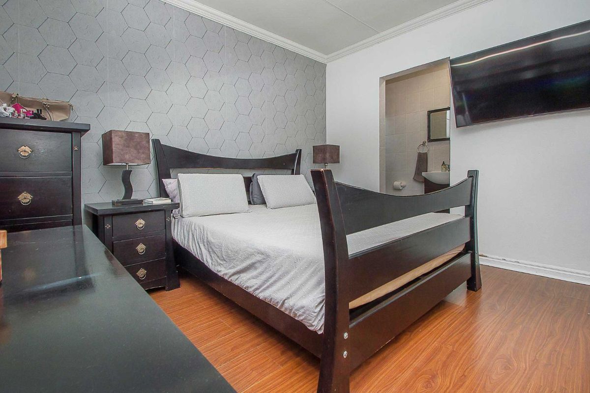 A bedroom featuring laminate flooring, a geometric patterned accent wall, and an en-suite bathroom with a wall-mounted basin.