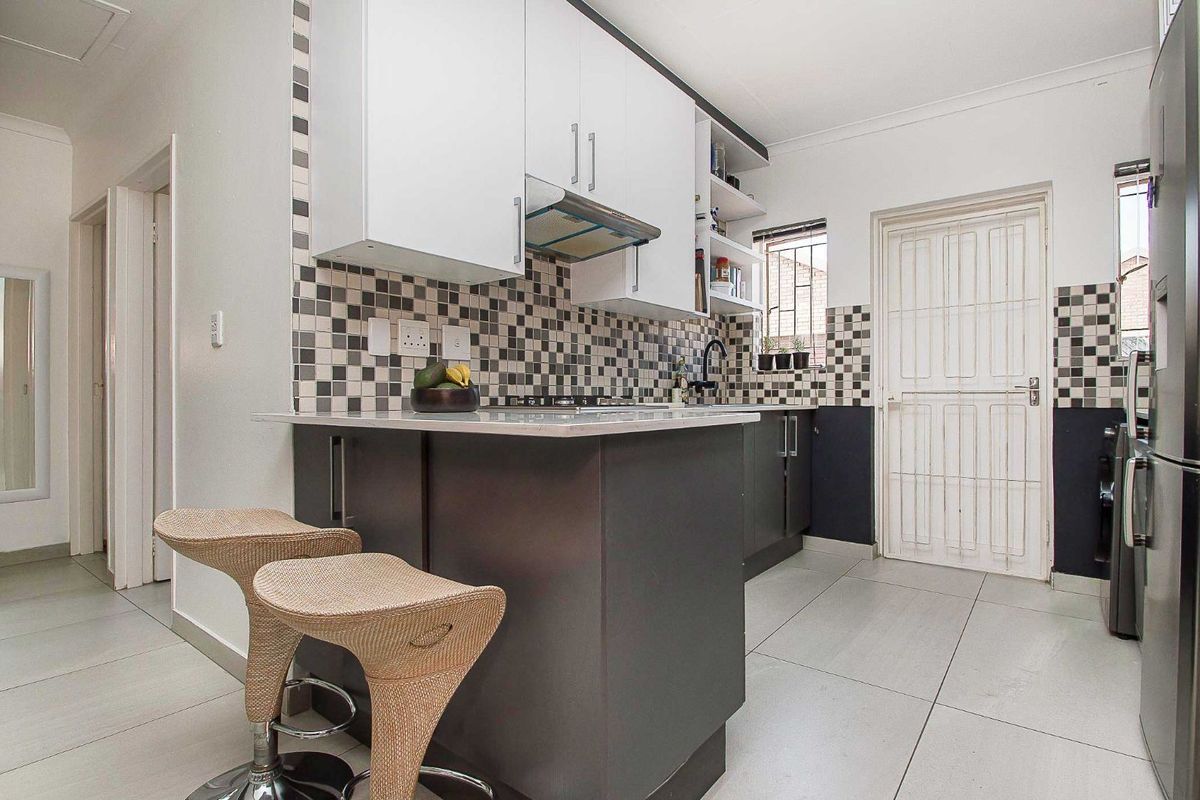 Modern kitchen featuring two-tone cabinetry, stone countertops, a built-in hob, extractor fan, and tiled flooring with a security gate leading outdoors.