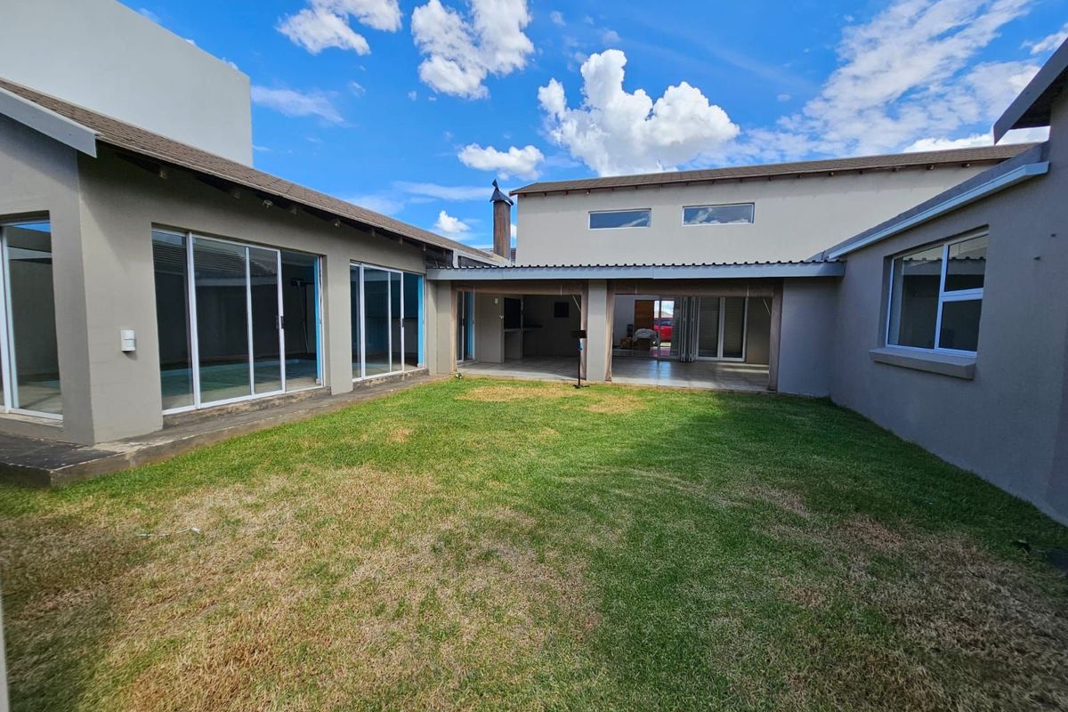 A spacious rear courtyard featuring a central lawn area, covered patio space, and large sliding glass doors providing seamless indoor-outdoor flow.