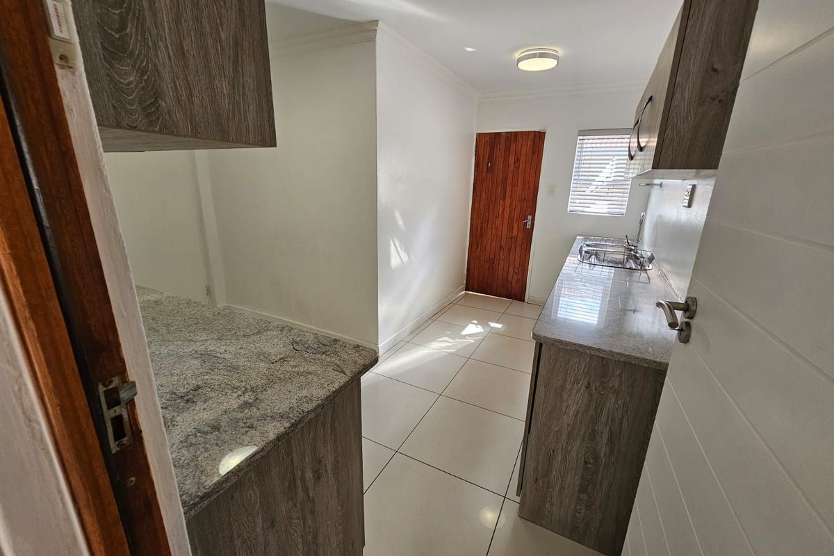 A functional kitchen featuring granite countertops, wood-look cabinetry, tiled flooring, and a rear door providing access to the exterior.