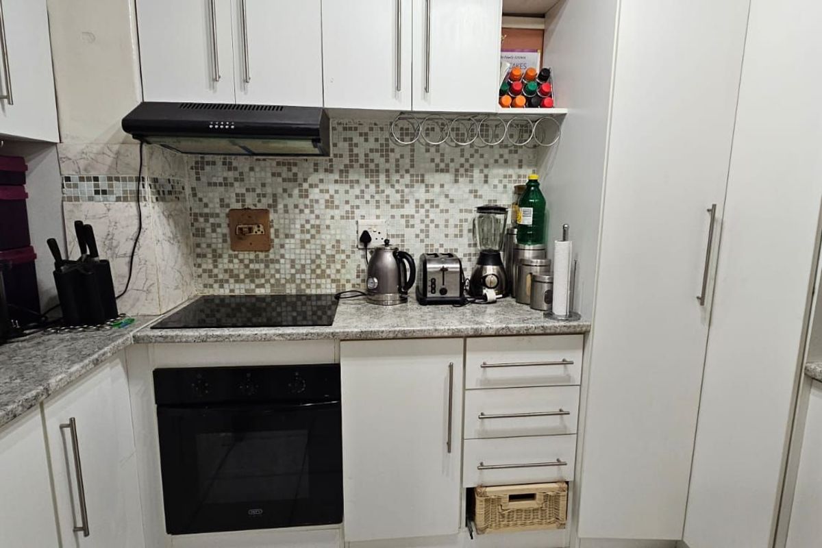 Compact kitchen featuring white cabinetry, granite-look countertops, mosaic tile backsplash, built-in oven, and extractor fan.