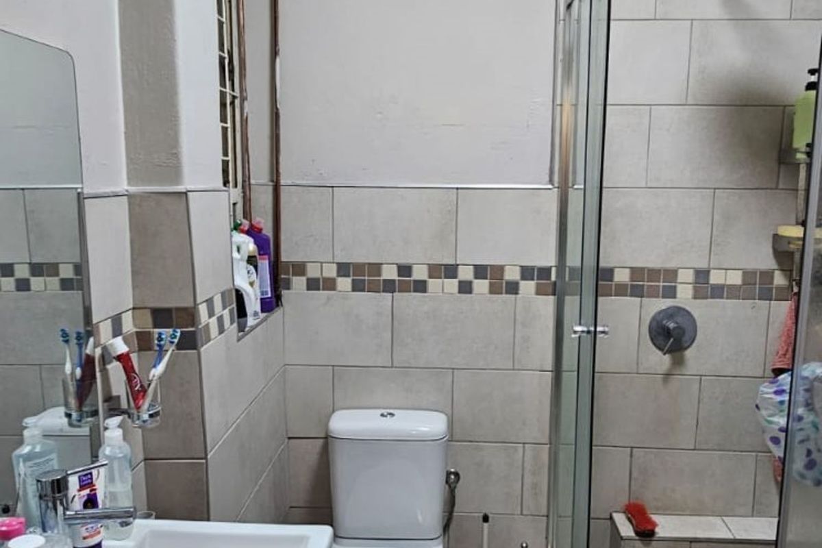 A compact bathroom featuring a glass-enclosed shower with pebble-style flooring, a wall-mounted basin, and a standard toilet with neutral wall tiling.