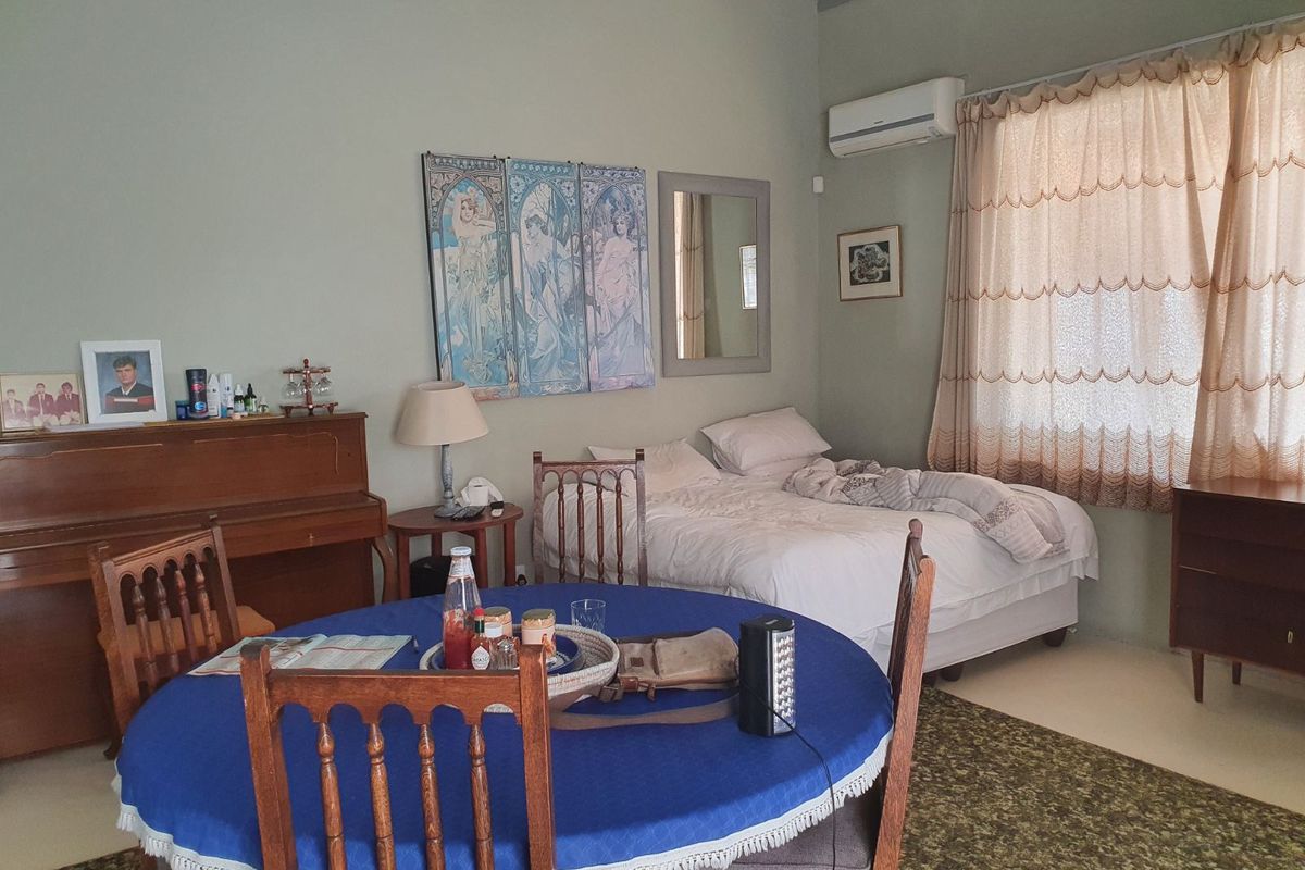 A bedroom featuring a split-system air conditioner and large window with curtains, providing a functional space with neutral wall tones.