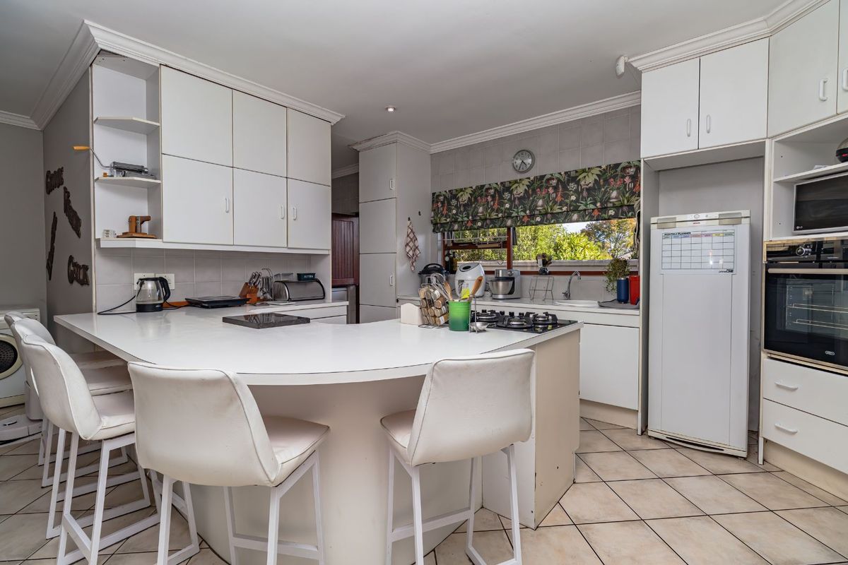 Functional kitchen featuring white cabinetry, a breakfast bar, built-in oven, gas hob, and tiled flooring with a window overlooking the garden.