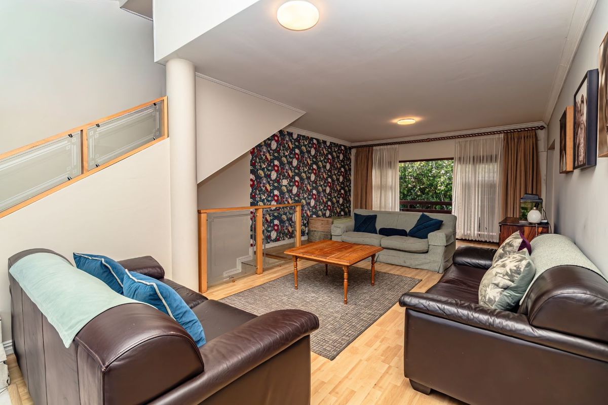 Spacious living room featuring light wood flooring, a feature wallpaper wall, and an open staircase with glass balustrades.