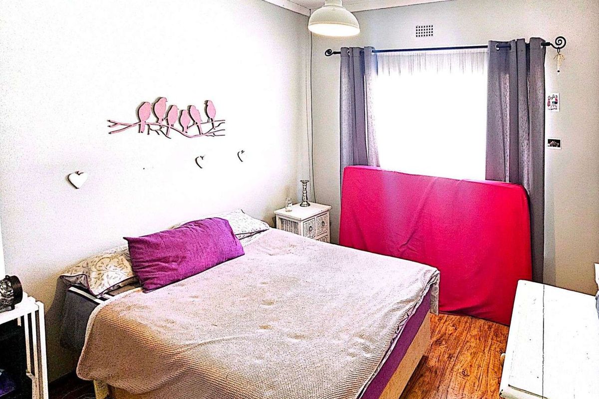A bedroom featuring wooden flooring, a window with curtain rods, and a central ceiling light fixture.