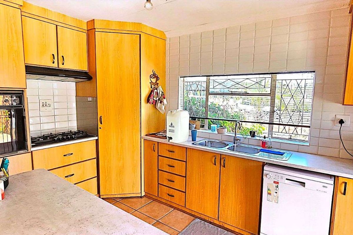 A functional kitchen featuring light wood cabinetry, tiled backsplash, built-in oven, gas hob, and a double sink with a window view.