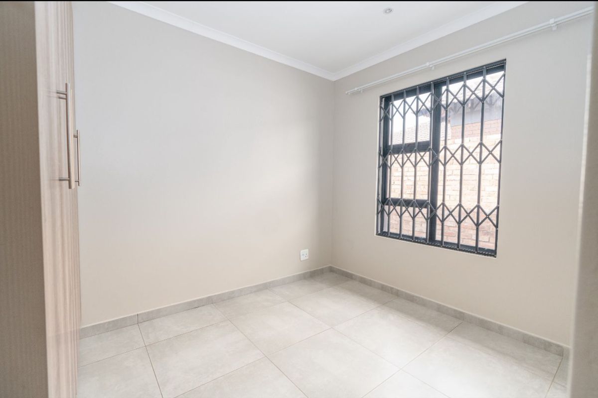 A bright, empty bedroom featuring neutral tiled flooring, built-in cabinetry, and a window fitted with security bars.