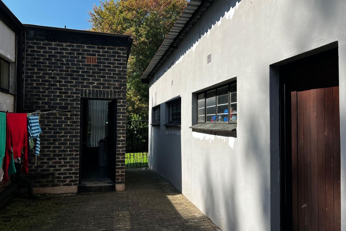 Exterior view of the property showing a paved side walkway between two building structures with exposed brick and painted wall finishes.