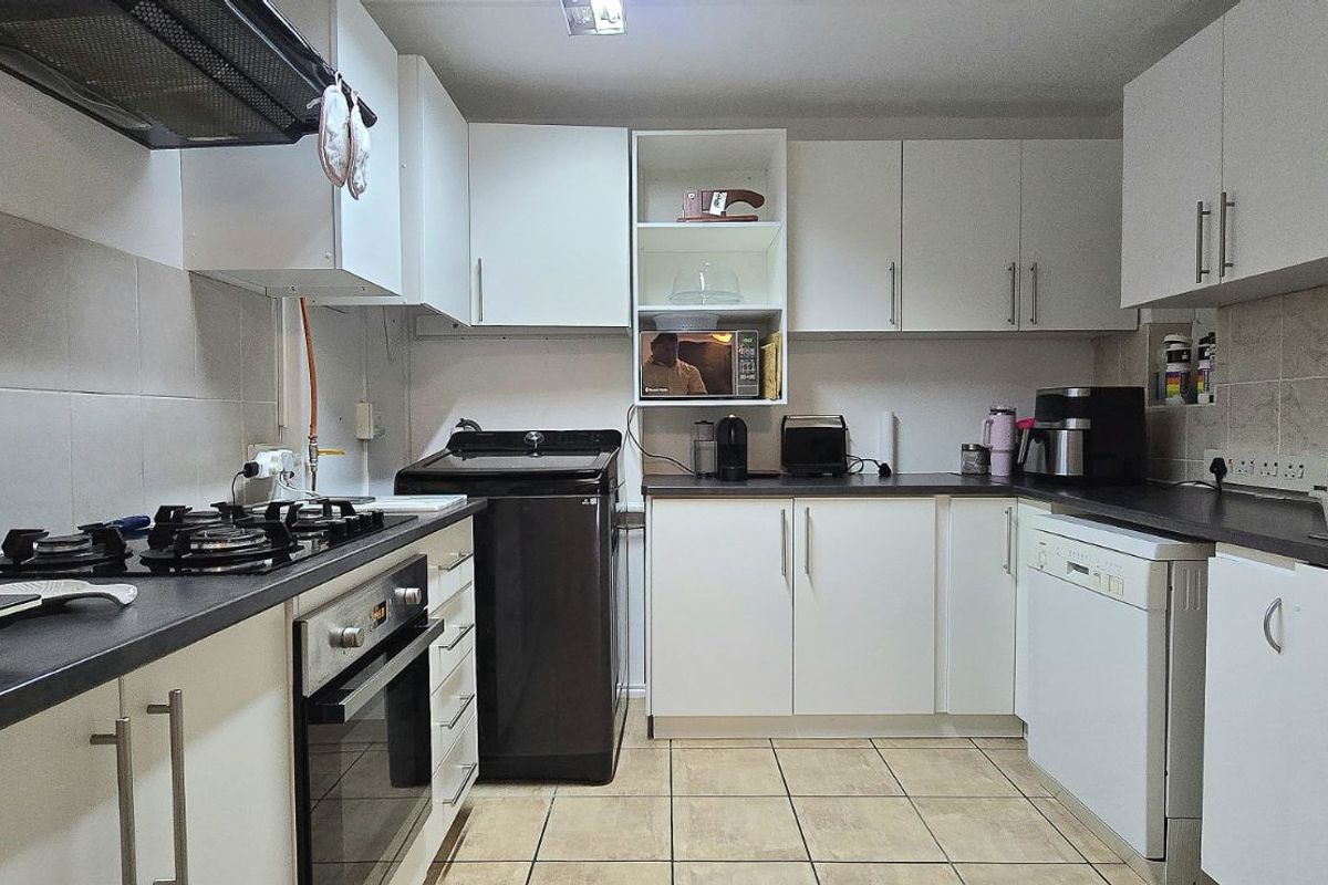 Functional kitchen featuring white cabinetry, dark countertops, built-in oven, gas hob, extractor fan, and tiled flooring.