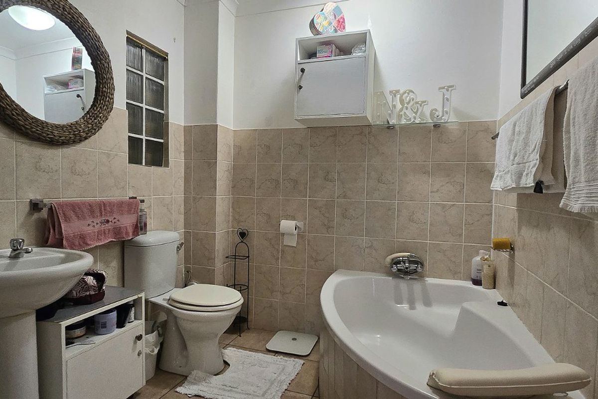 A functional bathroom featuring a pedestal basin, a corner bathtub, and neutral wall tiling throughout.