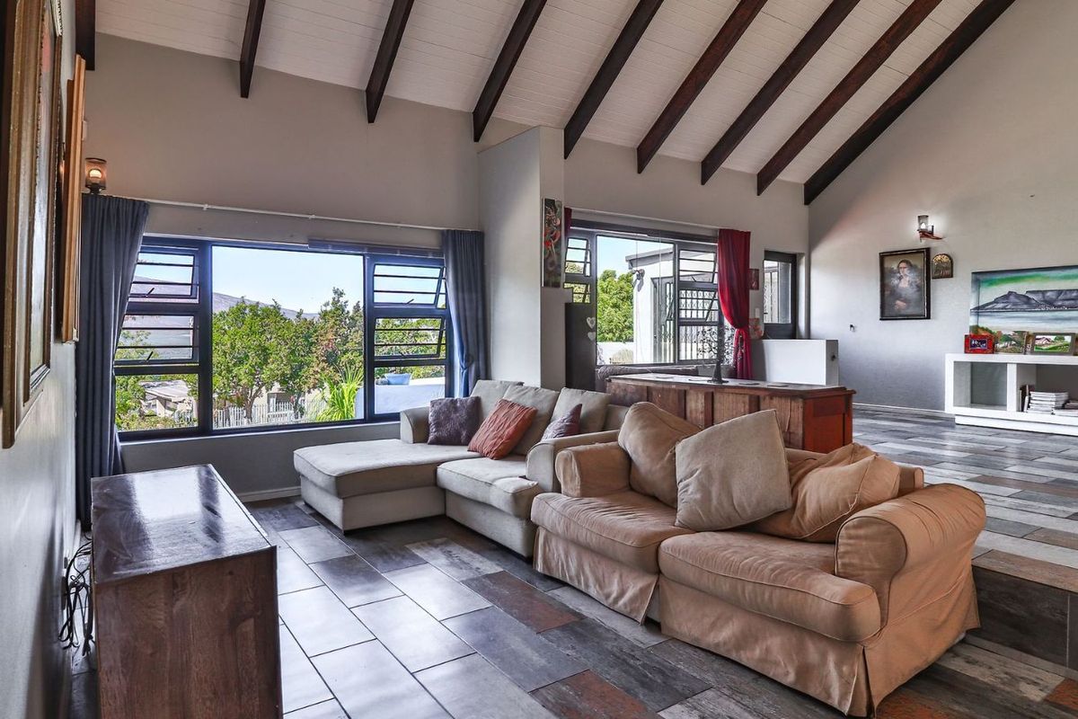 Spacious living area featuring high vaulted ceilings with exposed timber beams, large windows, and multi-toned tiled flooring.