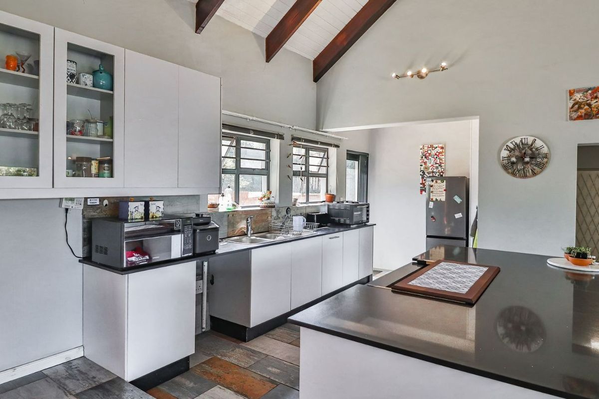 Modern kitchen featuring a large central island with dark stone countertops, ample cabinetry, and high vaulted ceilings with exposed timber beams.