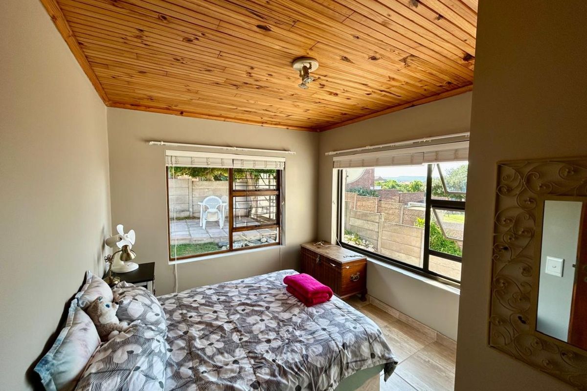 A bedroom featuring a natural wood-paneled ceiling, tiled flooring, and large windows providing natural light and views of the rear garden area.