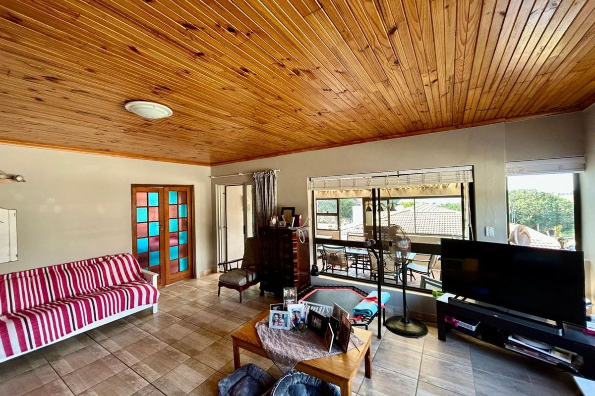 Spacious living room featuring a distinctive timber-clad ceiling, tiled flooring, and large windows providing natural light and access to an outdoor patio area.
