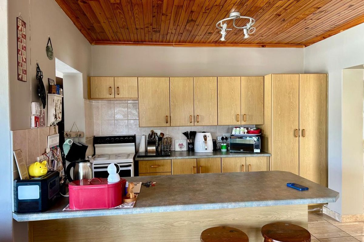 A functional kitchen featuring light wood cabinetry, a breakfast bar, tiled backsplash, and a distinctive timber-paneled ceiling.