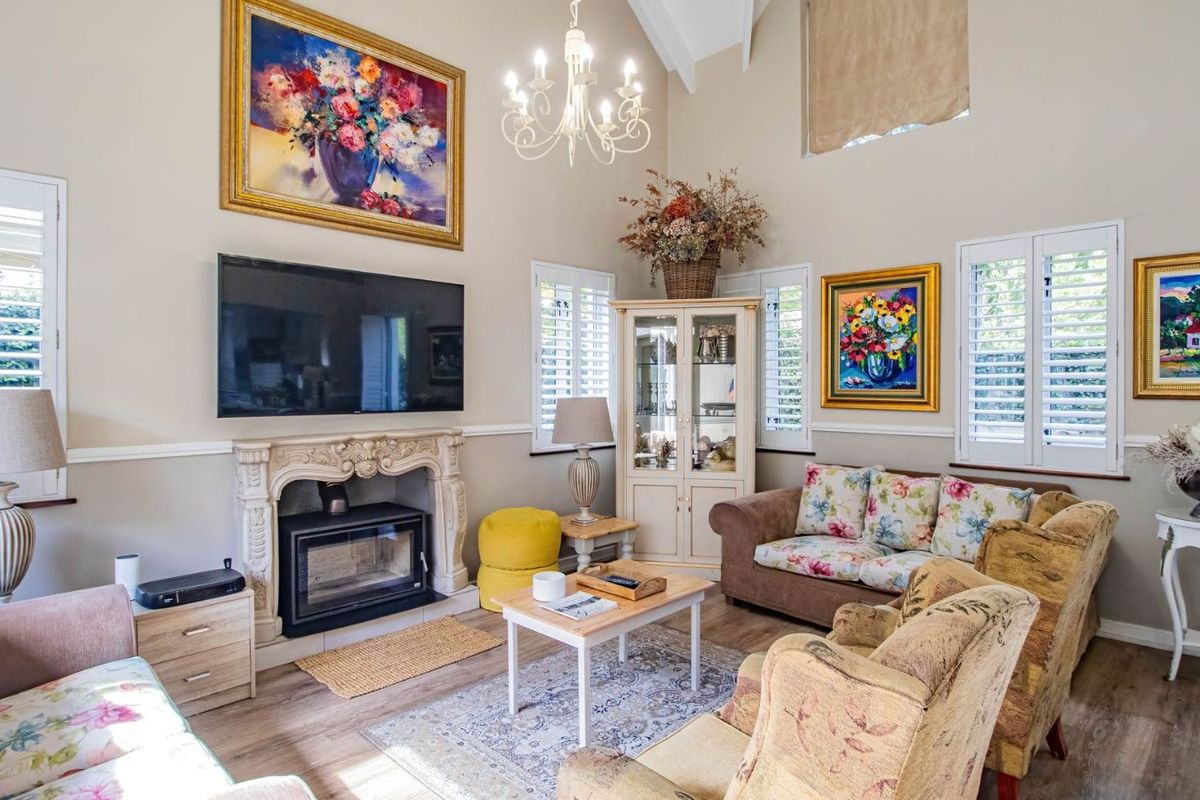 A bright living room featuring a vaulted ceiling, a classic stone fireplace with an integrated wood-burning stove, and plantation shutters on the windows.