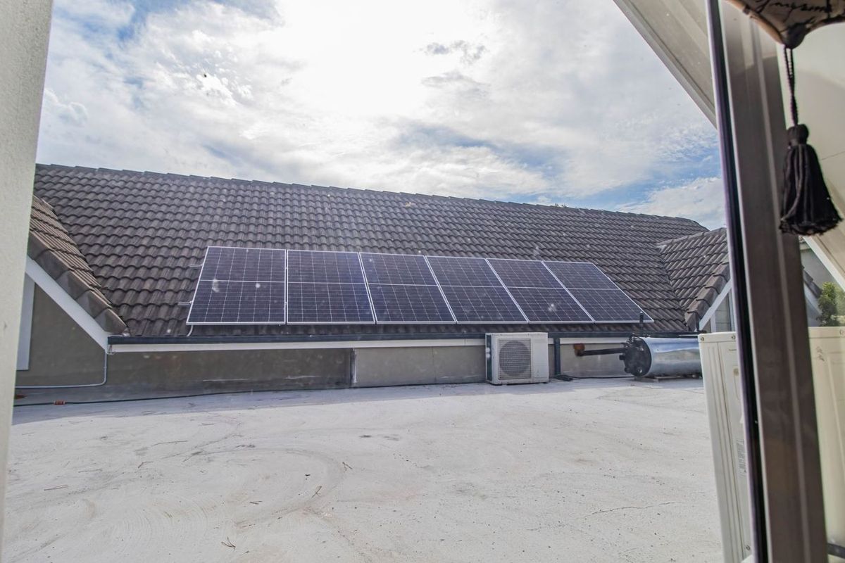 View of a flat roof area featuring solar panels, an air conditioning condenser unit, and a solar water heater geyser.