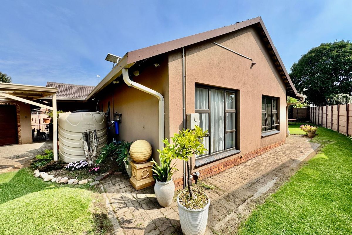 Rear exterior view of the house featuring a paved walkway, landscaped garden area, and a large water storage tank.
