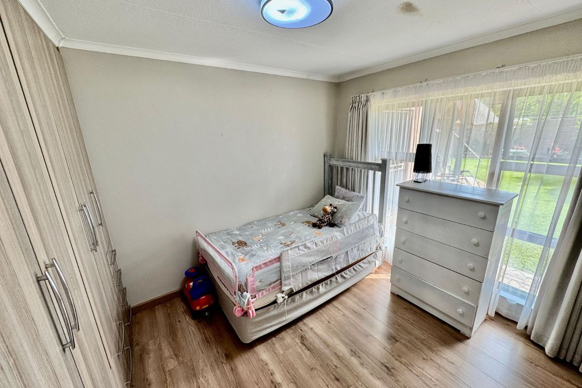 A bedroom featuring wood-look laminate flooring, built-in cupboards, and sliding glass doors providing access to the garden.
