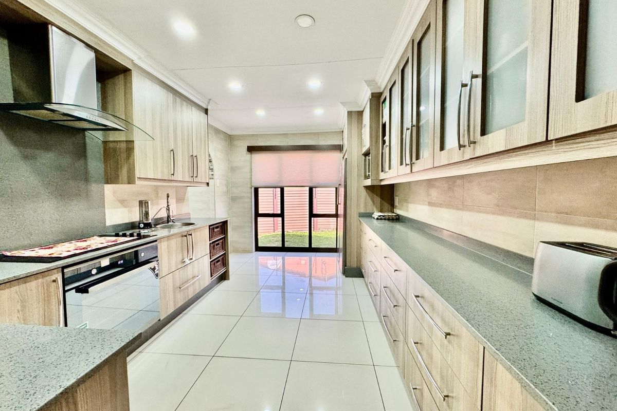 Modern galley-style kitchen featuring light wood cabinetry, stone countertops, integrated oven, extractor fan, and polished floor tiles with direct access to the rear garden.