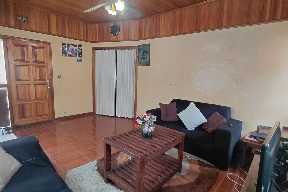 A living room featuring tiled flooring, timber ceiling paneling, and a ceiling fan, offering a dated aesthetic ready for modernization.