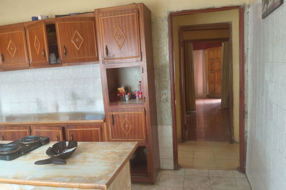 A dated kitchen featuring wood-finish cabinetry, tiled walls, and a central island, with a doorway leading to an adjacent hallway.