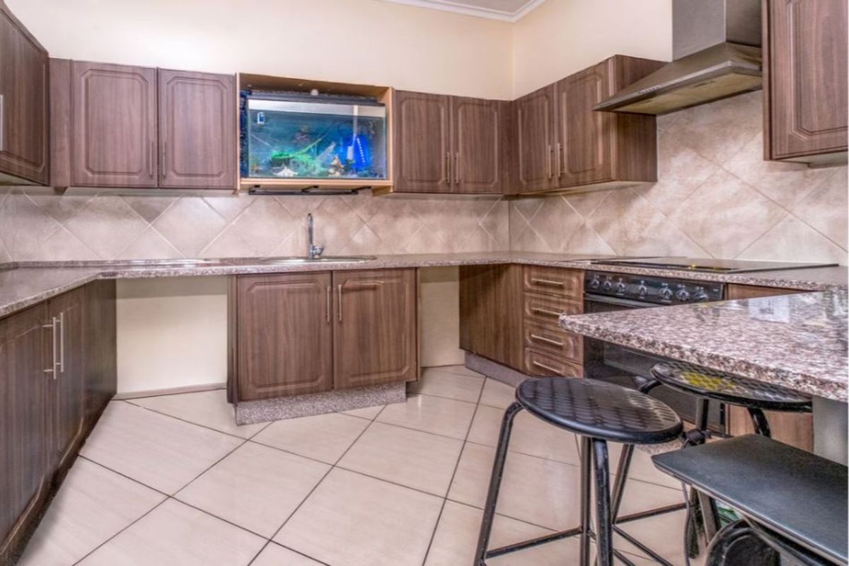 A functional kitchen featuring wood-finish cabinetry, granite-style countertops, a built-in oven with extractor fan, and tiled flooring.