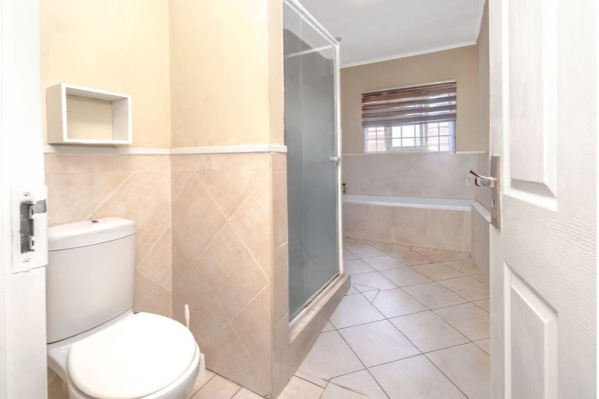 A functional bathroom featuring a separate shower enclosure, a bathtub, and a toilet with neutral wall and floor tiling.