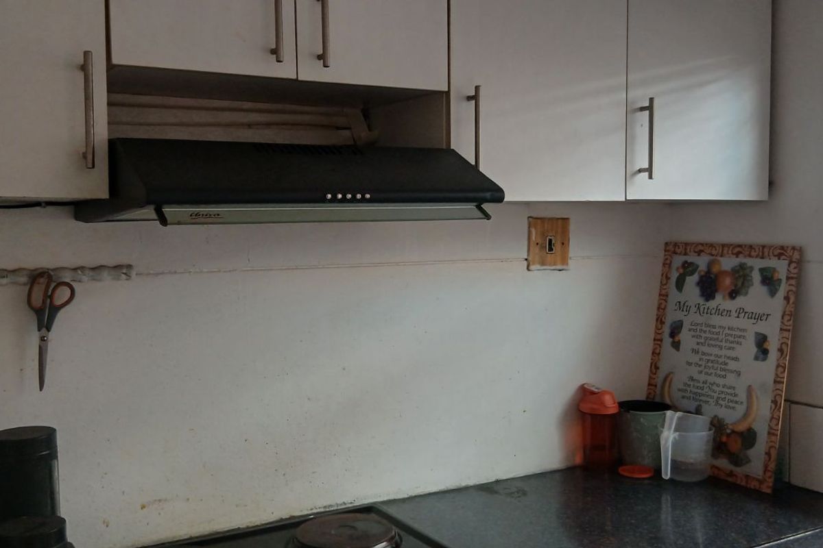 A functional kitchen area featuring white cabinetry, a built-in extractor fan, and a dark countertop with tiled splashback.