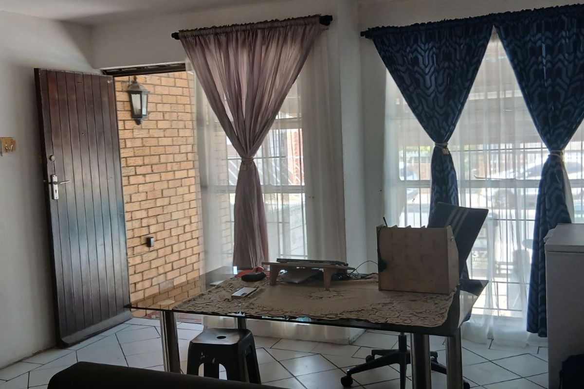 A functional living area featuring tiled flooring, large windows with curtains, and direct access to an exterior brick-walled entrance area.