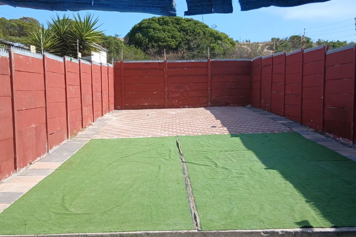 A private, enclosed outdoor courtyard featuring paved sections, artificial turf, and high perimeter boundary walls with security spikes.
