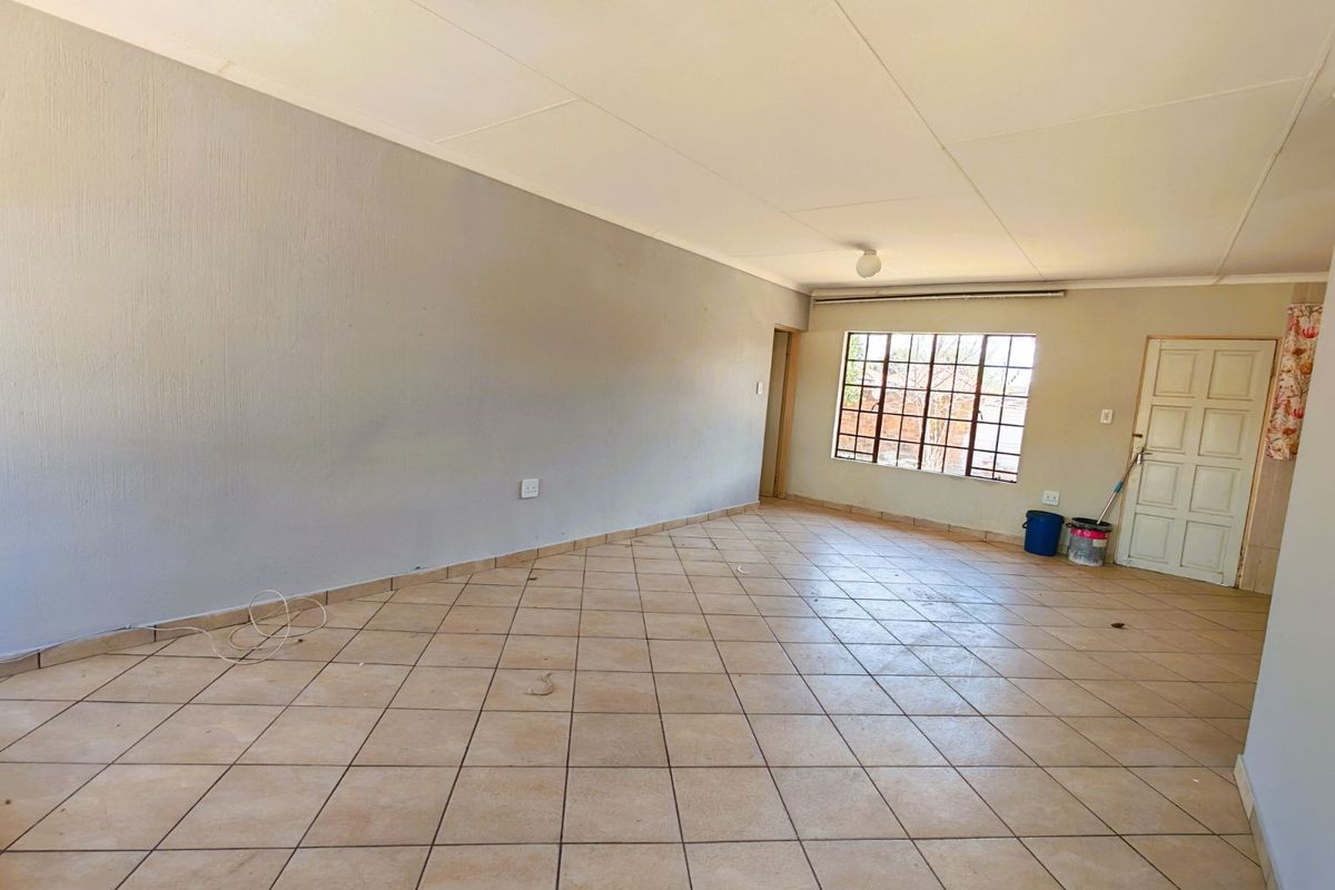 A spacious, empty living area featuring neutral tiled flooring, large windows for natural light, and a simple, functional layout ready for personalization.