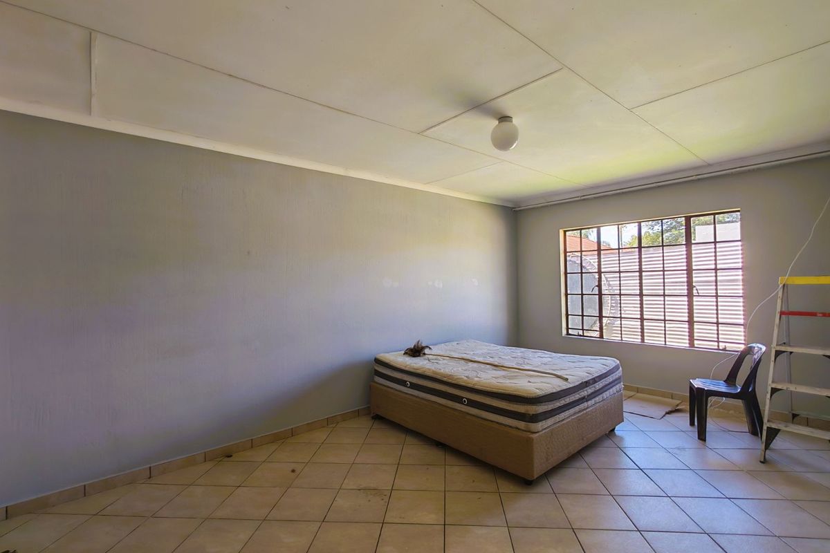 A spacious bedroom featuring tiled flooring, a large window with security bars, and a simple ceiling finish.