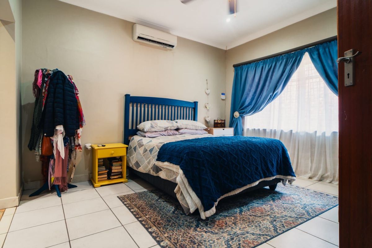 A bedroom featuring tiled flooring, a wall-mounted air conditioning unit, and a window with curtain tracks.