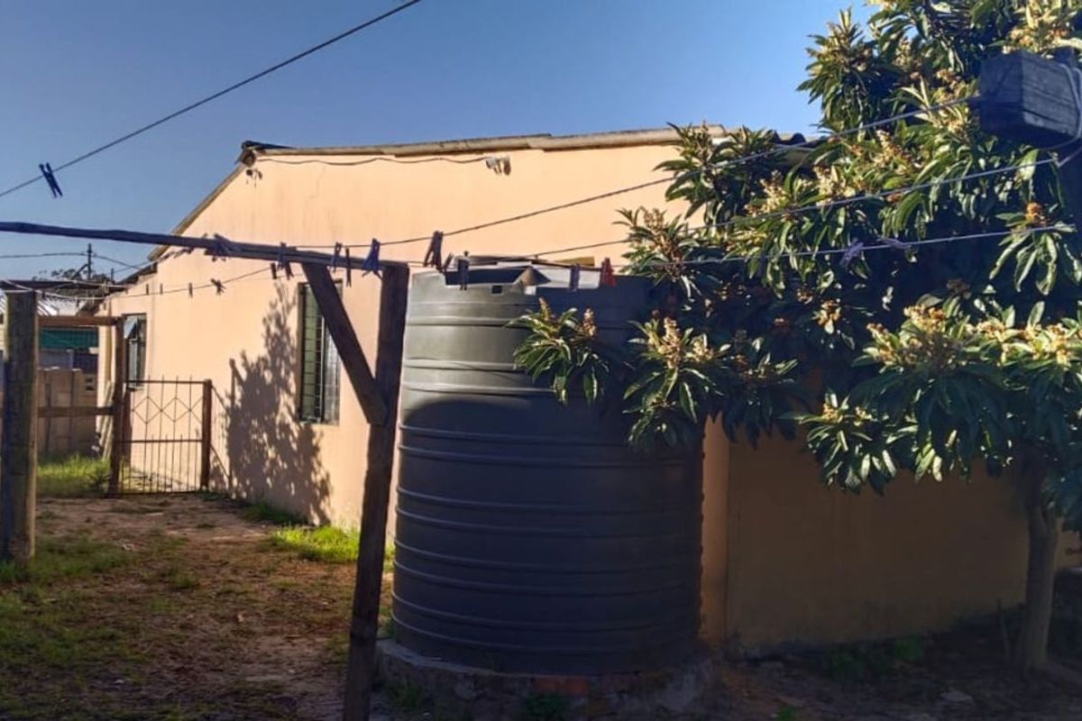 Rear exterior view of the property featuring a water storage tank, established tree, and outdoor utility area with a clothesline structure.