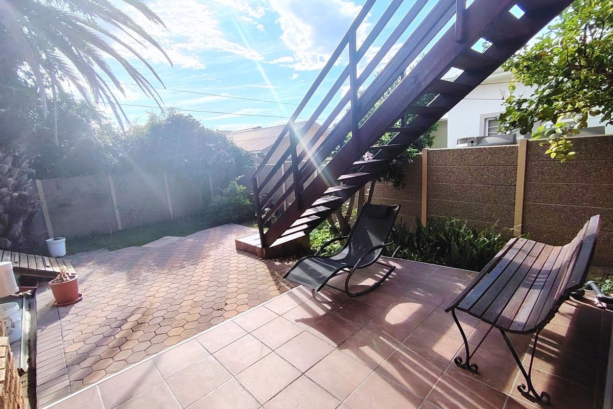 A private rear courtyard featuring paved flooring and an external timber staircase leading to an upper level, set within a walled garden area.