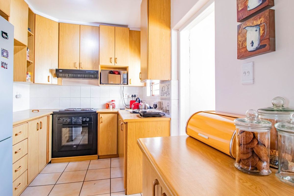 A functional kitchen featuring light wood cabinetry, tiled flooring, and built-in oven and extractor fan.