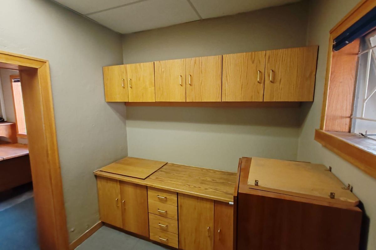 A functional office kitchenette area featuring built-in wooden cabinetry, laminate countertops, and a drop ceiling, providing practical storage and workspace.