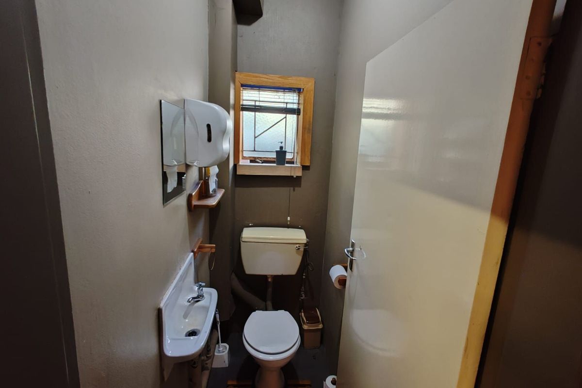 A compact, functional office restroom featuring a wall-mounted basin, toilet, and a small window with wooden trim.