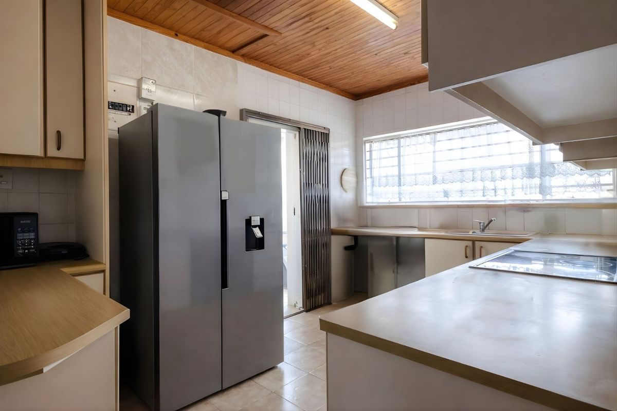Functional kitchen featuring built-in cabinetry, laminate countertops, integrated hob, and tiled flooring with a timber-paneled ceiling.