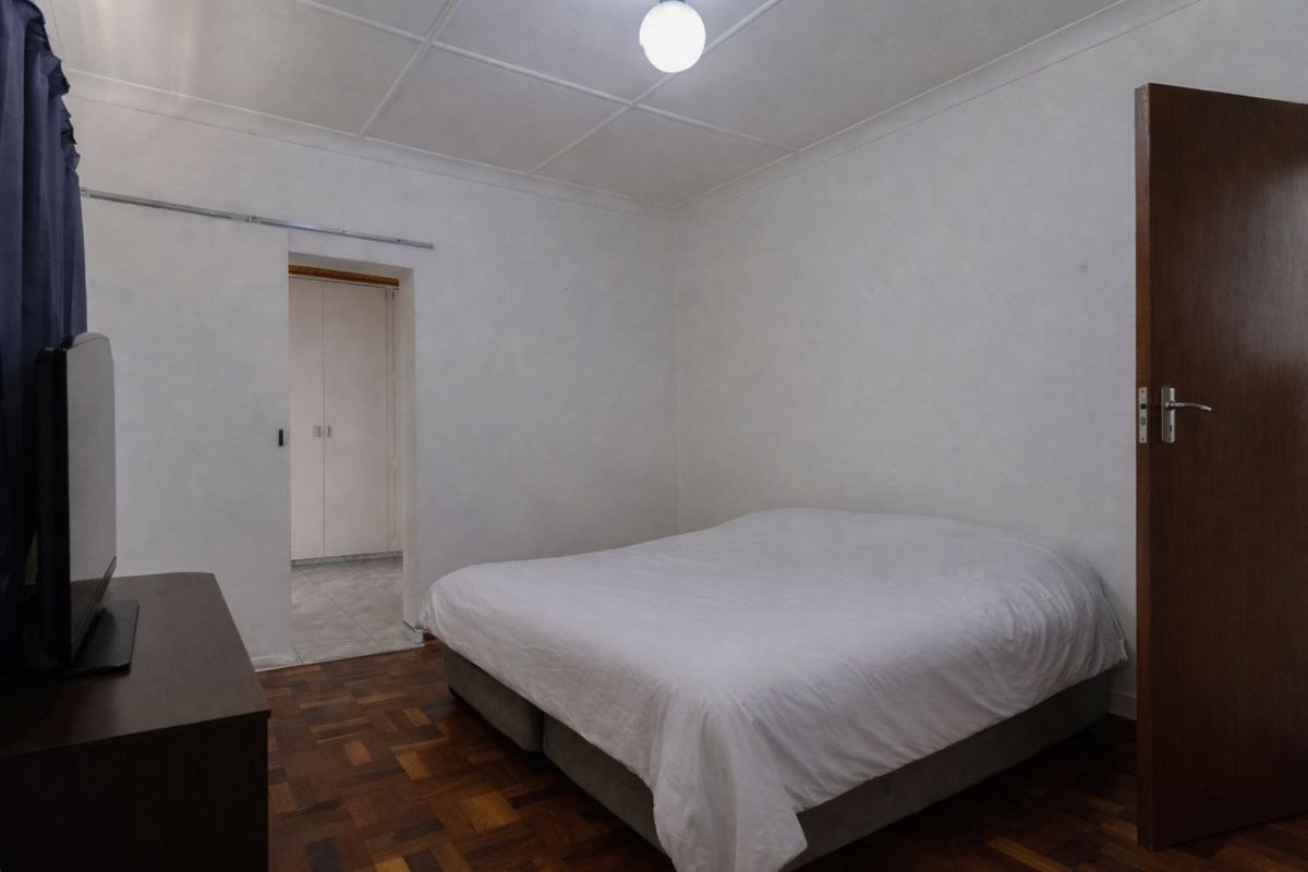 A simple bedroom featuring parquet flooring, a ceiling light fixture, and an adjacent walk-in closet area.