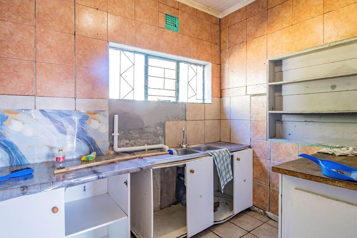 A dated kitchen area featuring tiled walls, a stainless steel sink, and open cabinetry requiring renovation and repair.