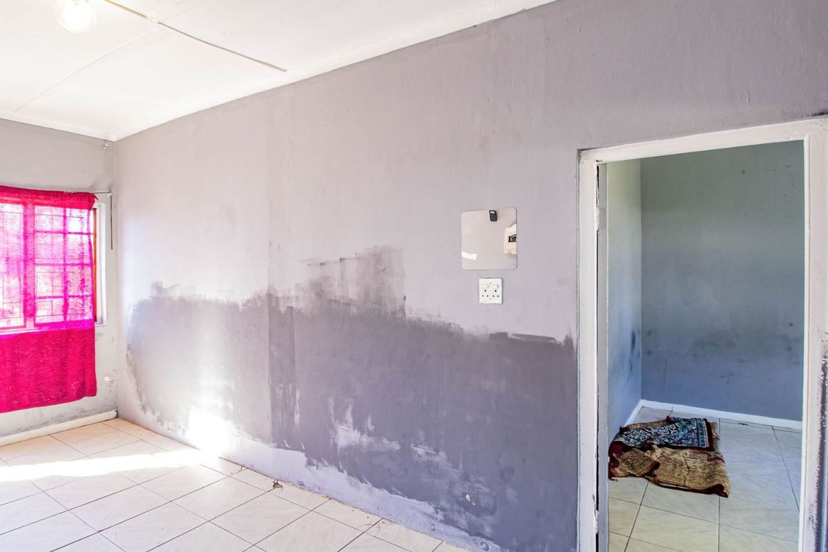 An interior room featuring tiled flooring and a doorway leading to an adjacent space, currently showing signs of incomplete wall painting and surface wear.