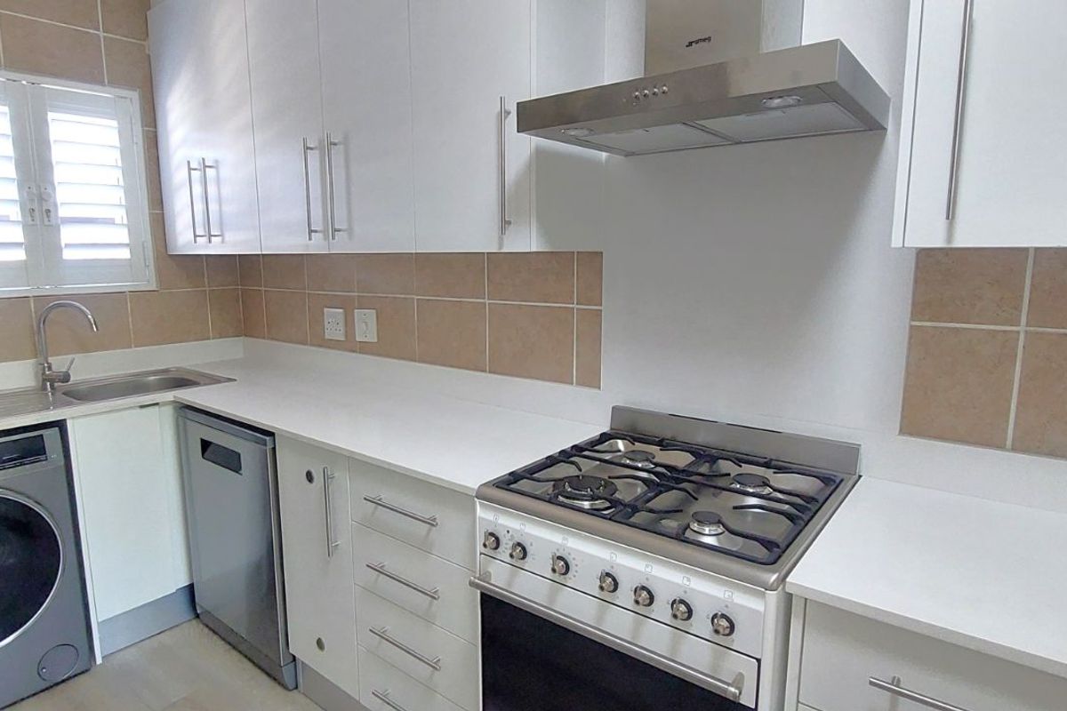 A functional kitchen featuring white cabinetry, stone-look countertops, a gas stove with extractor fan, and integrated space for laundry and dishwasher appliances.
