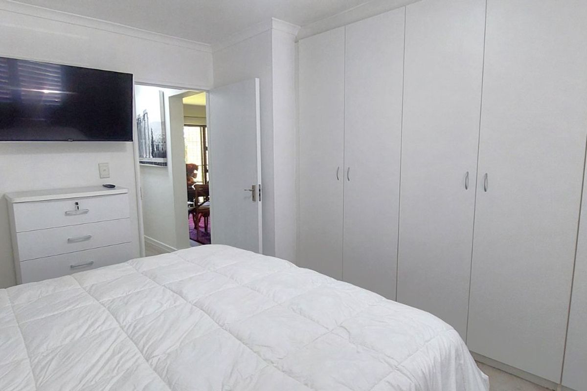 A bright bedroom featuring extensive floor-to-ceiling built-in wardrobes and neutral finishes, providing ample storage space.