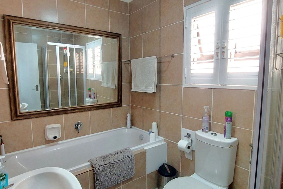 A functional bathroom featuring a bathtub, toilet, and vanity mirror with neutral wall tiling and natural light from a window.