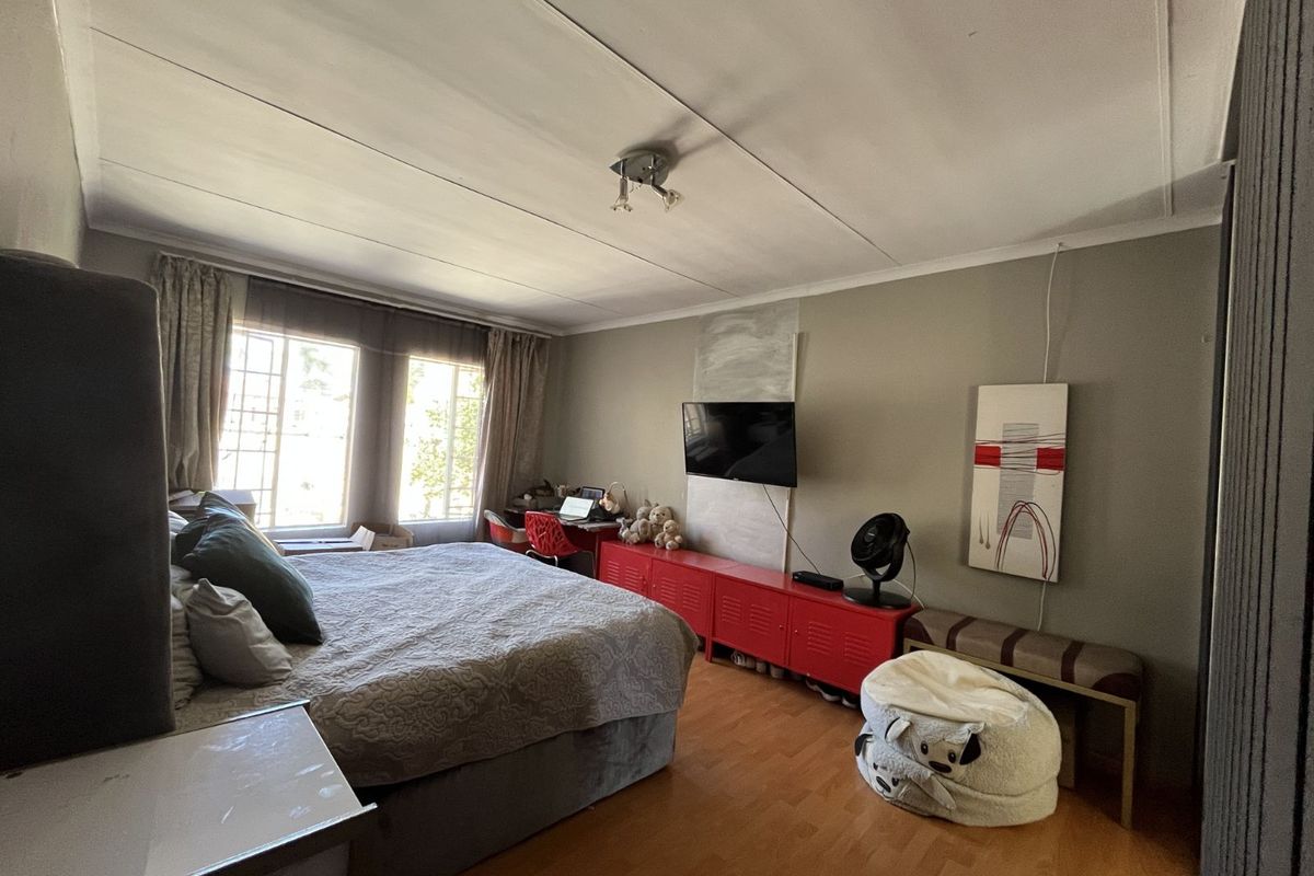 A spacious bedroom featuring laminate flooring, large windows allowing natural light, and a neutral wall palette.