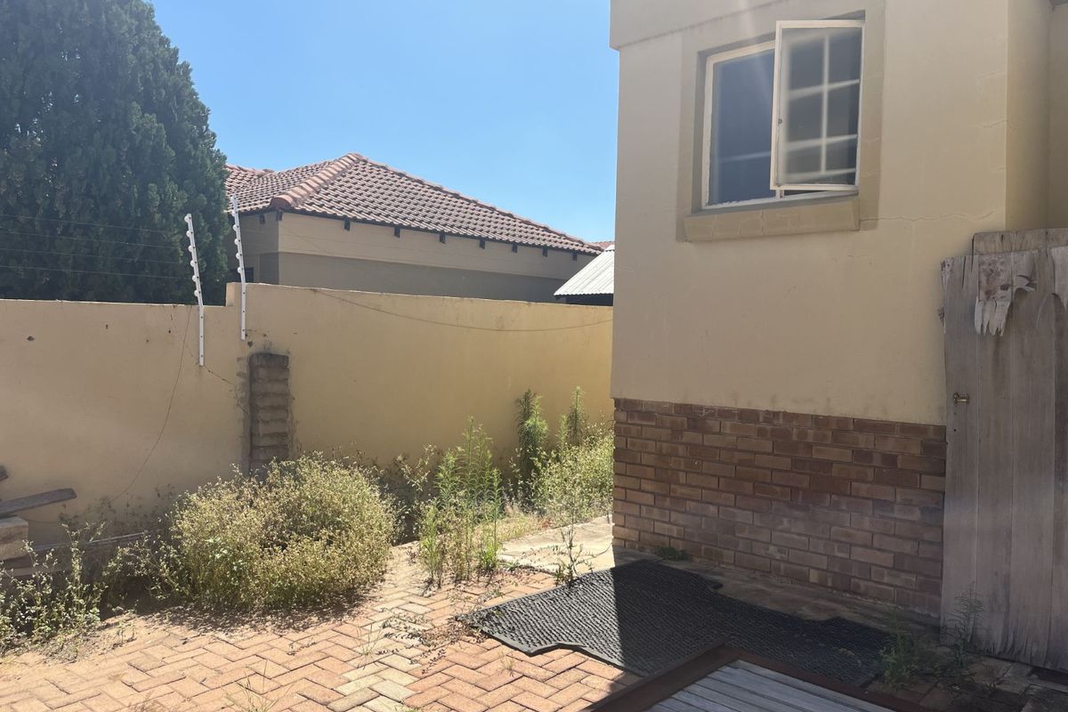 A rear exterior view of the property featuring paved ground, a perimeter wall with electric fencing, and a side entrance with a weathered gate.