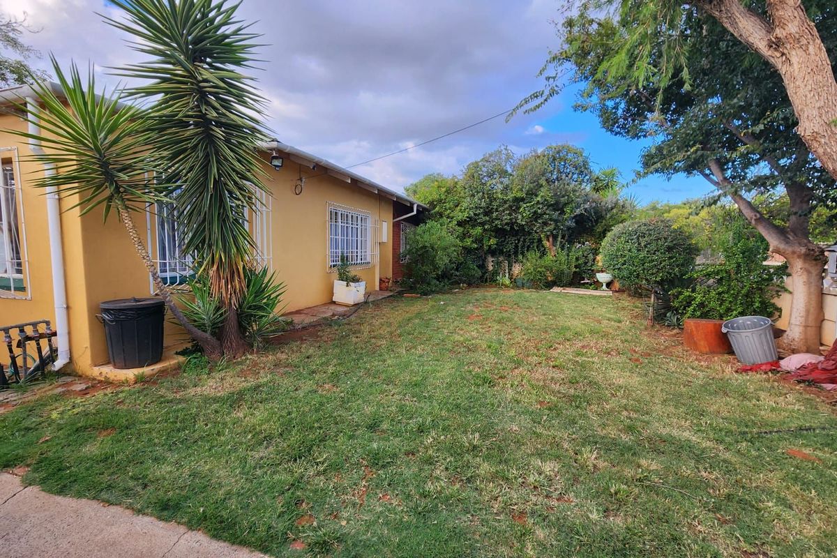 A view of the rear garden and backyard area featuring established trees, lawn, and the rear facade of the house.